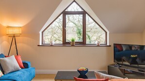 Una sala de estar con un ventanal grande, televisor, sofá, mesa de centro y lámpara de pie.