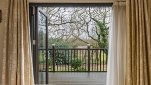 Una habitación con un amplio ventanal corredero que da a un balcón exterior con vistas a árboles y una valla.