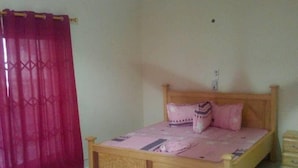 A bedroom with a wooden bed, a ceiling fan, and a red curtain. - Nyaboa Hotel (Kumasi)