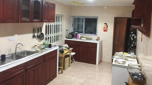 A compact kitchen with wooden cabinets, a sink, and a window. - Nyaboa Hotel (Kumasi)