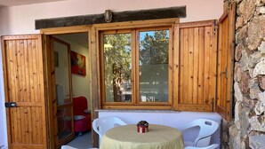 A small patio with a round table and four white plastic chairs, a red sofa, and a wooden door leading to an interior room. - Appartamento Rosa La Cinta (San Teodoro)