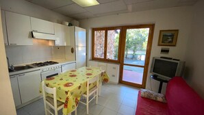 A compact kitchen with a dining table, a red sofa, and a television. - Appartamento Rosa La Cinta (San Teodoro)