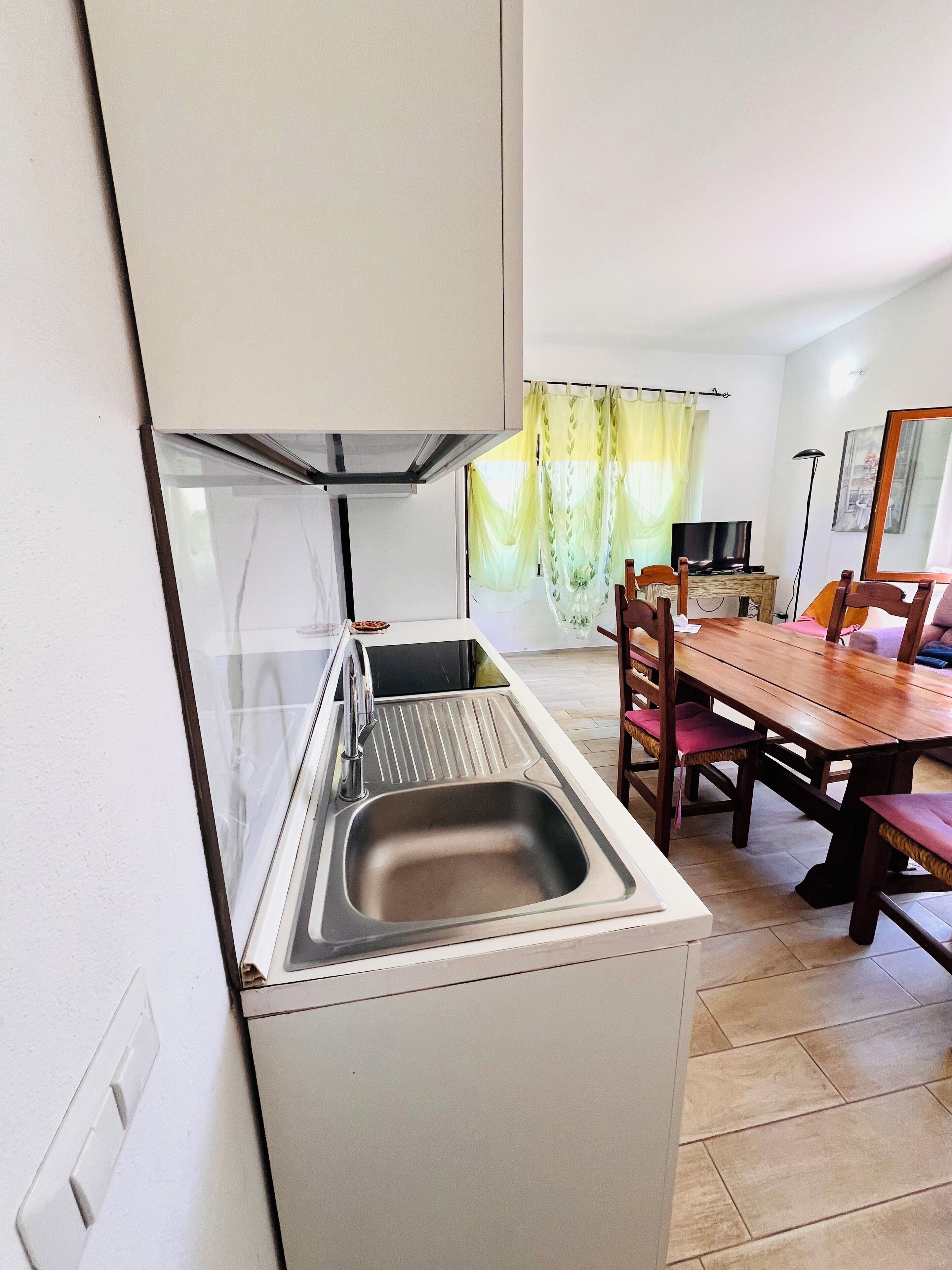Een kleine keuken met een spoelbak, een eettafel met stoelen en een televisie op de achtergrond.