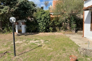 A grassy yard with a lamp post, a potted plant, and a white building with a red roof.