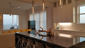 A modern kitchen with a large island, pendant lights, and a view of the ocean.