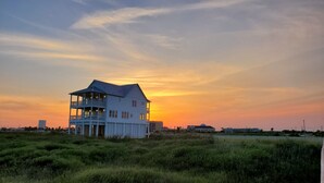 A two-story white house with a balcony, set against a sunset sky.