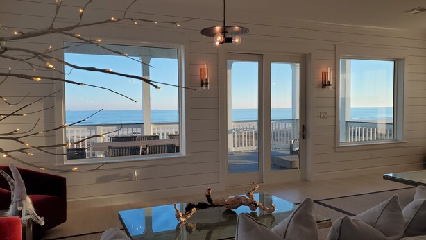 A spacious room with large windows overlooking the ocean, a glass-top table, and a red chair.