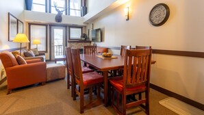 A dining area with a wooden table and chairs, a sofa, and a lamp. - 2 Bedrooms | Mountain Views l AC (Fernie)