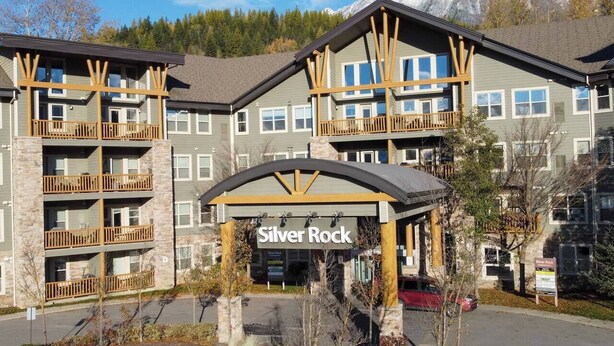 A multi-story hotel with balconies, a covered entrance, and a mountainous backdrop. - 2 Bedrooms | Mountain Views l AC (Fernie)