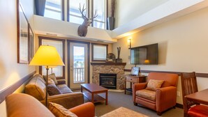 A cozy living room with a fireplace, comfortable seating, and a mounted deer head. - 2 Bedrooms | Mountain Views l AC (Fernie)