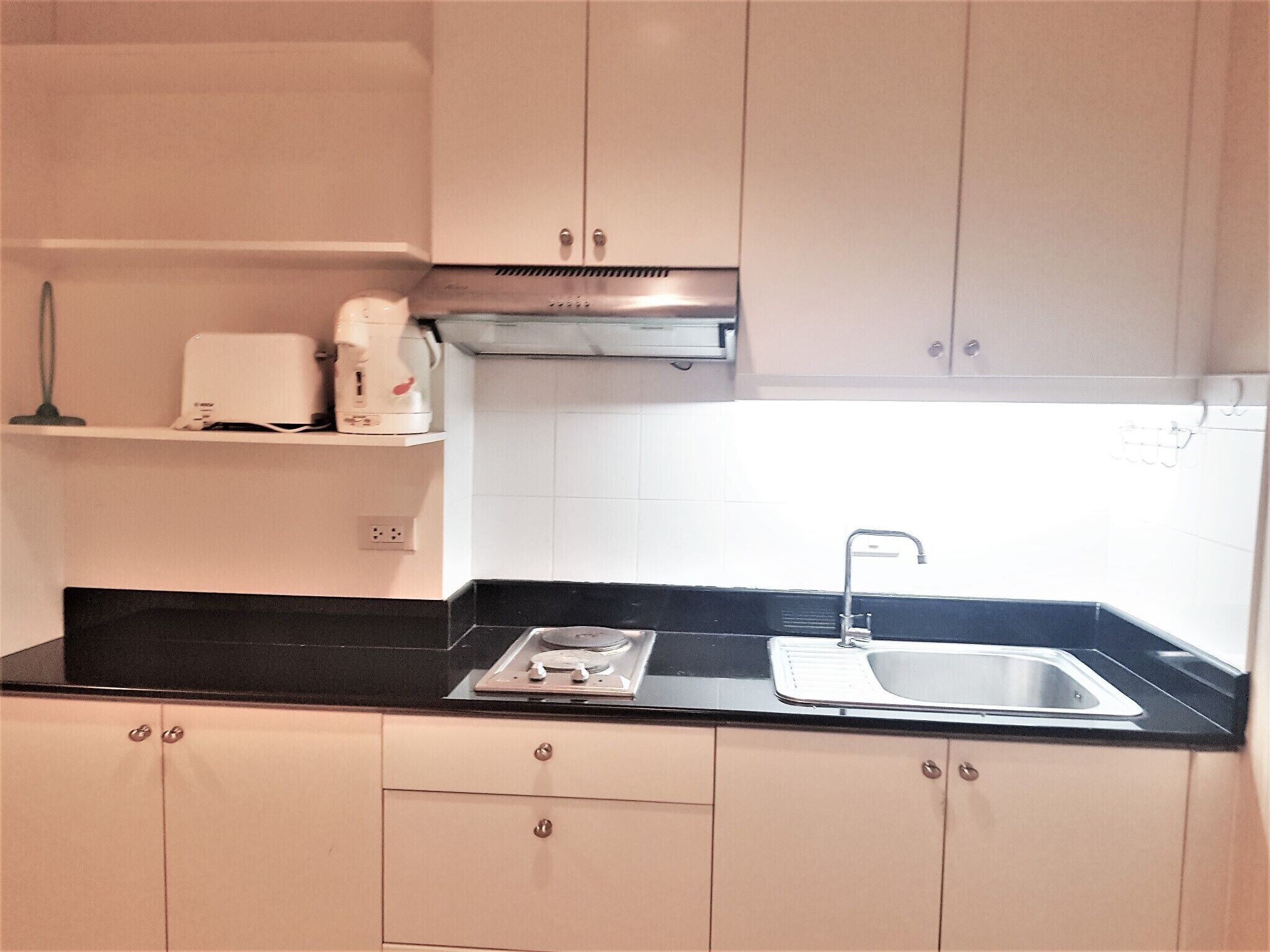A compact kitchen with a black countertop, a stainless steel sink, and beige cabinets.
