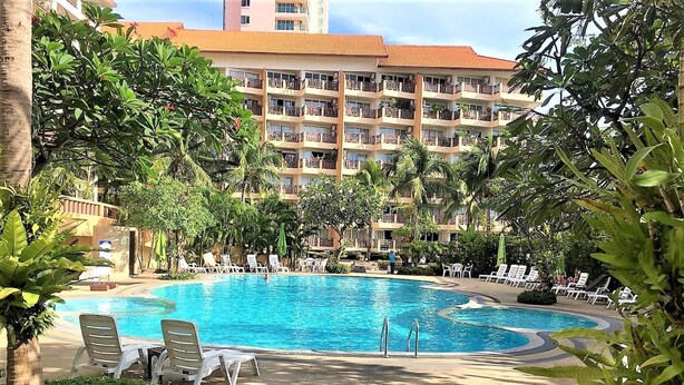 A hotel pool area with a large pool, lounge chairs, and palm trees. - Royal Hill Resort Pattaya Corner Condo With sea & Pool Views (Pattaya)
