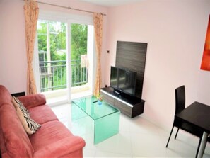 A living room with a sofa, a glass coffee table, a flat-screen TV, and a balcony with curtains.