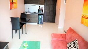 Een compacte leefruimte met een kitchenette, een eethoek en een zithoek met een bank.