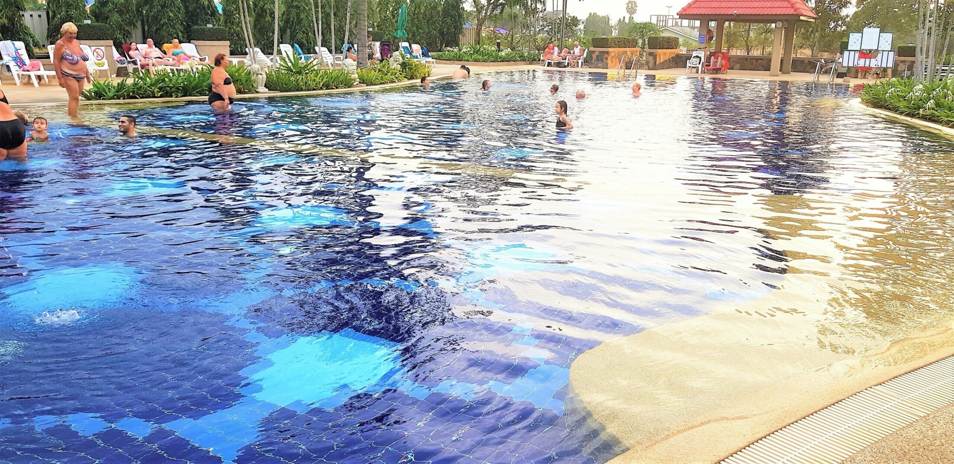 Una piscina con suelo de baldosas y un área de descanso con sillas y sombrillas alrededor.