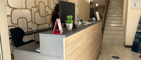 A reception desk with a patterned wall, a potted plant, and a sign prohibiting smoking.