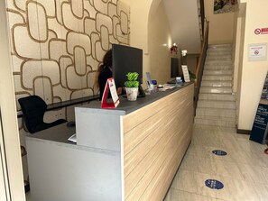 Un comptoir d'accueil avec un mur décoré, une plante en pot et un panneau indiquant qu'il est interdit de fumer.