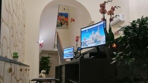 A modern reception area with a glass desk, two monitors, a chandelier, and potted plants. - 55 Aira (Palermo)