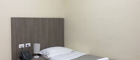 A single bed with a grey headboard, a bedside table with a phone and lamp, and an air conditioner mounted on the wall.