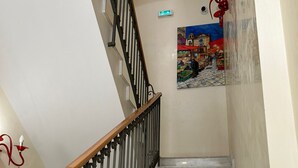 A marble staircase with a wooden handrail and black metal balusters, leading to a landing with a colorful mural of a market scene. - 55 Aira (Palermo)