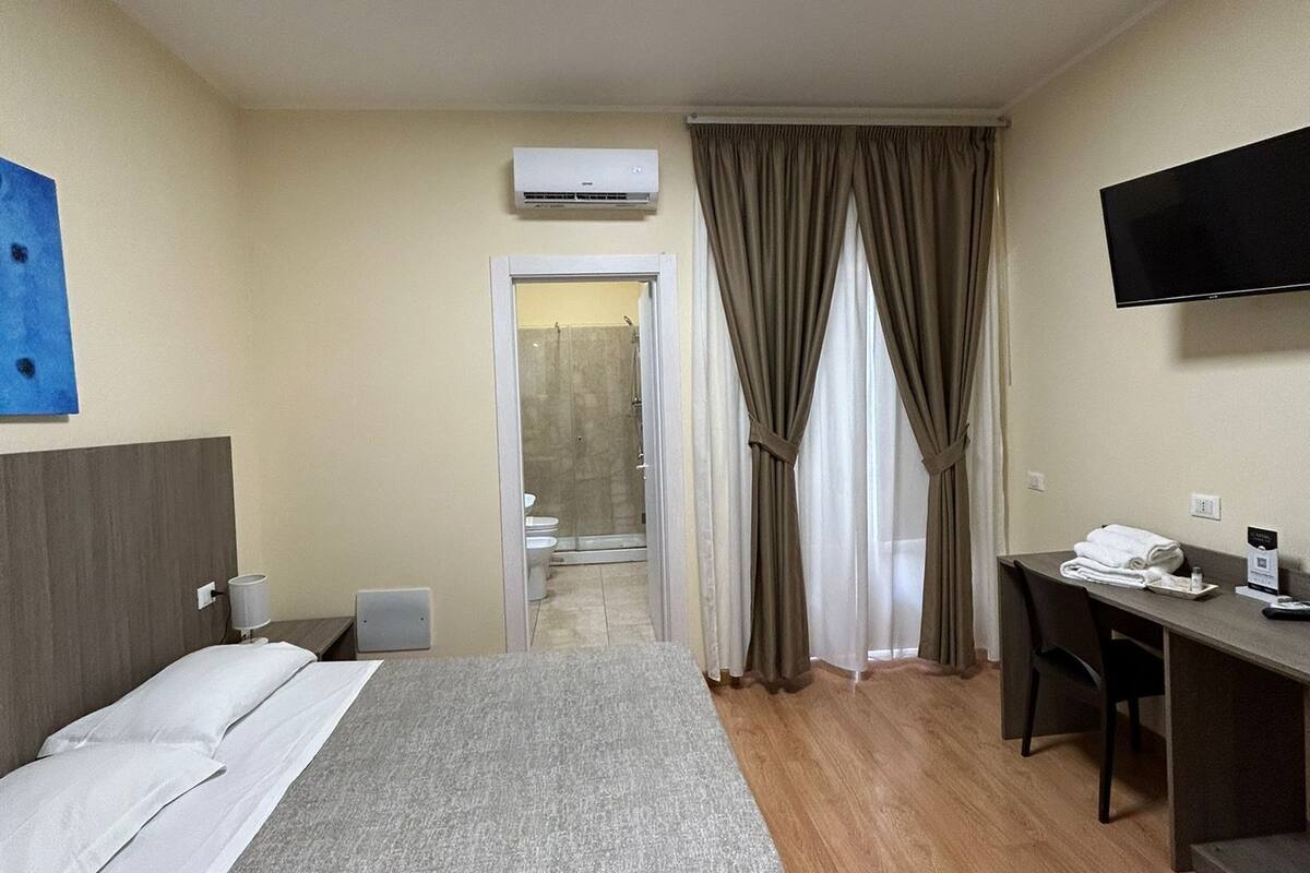 Una habitación de hotel con cama, escritorio, televisión y aire acondicionado.