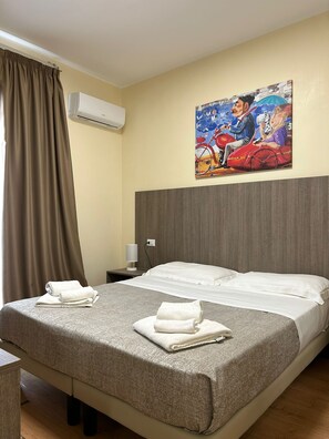 Une chambre d’hôtel avec un lit, une table de chevet, une lampe, un tableau au mur et une fenêtre avec des rideaux.