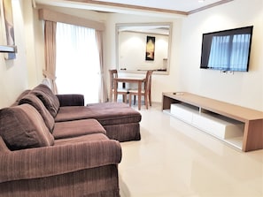 Una sala de estar moderna con un sofá seccional marrón, una mesa de comedor con sillas y un televisor de pantalla plana montado en la pared.