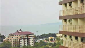 A multi-story building with balconies, a view of the sea, and a park area with trees. - Room-sea View Apartment Jomtien Beach co (Pattaya)