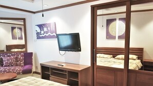 A hotel room with a bed, a TV, a sofa, and a wooden wardrobe.