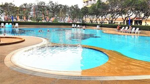 A swimming pool with multiple lanes, surrounded by lounge chairs and a landscaped area with trees. - Jomtien Beach Condominium 5th Floor Modern Studio Apartment Pattaya (Pattaya)