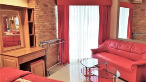A hotel room with a brick wall, a red leather sofa, a glass coffee table, a wooden desk with a mirror, and a red curtain. - Jomtien Beach Condominium 5th Floor Modern Studio Apartment Pattaya (Pattaya)