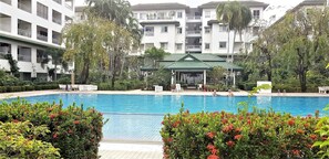 Relax by the serene pool surrounded by lush greenery and a multi-story building with balconies.