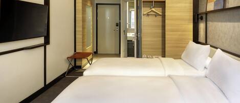 A hotel room with two beds, a TV, a coat rack, and a door leading to a bathroom.