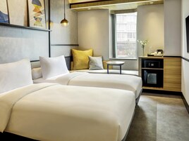 Habitación de hotel con dos camas, una mesita, microondas y ventana con vistas a edificios.