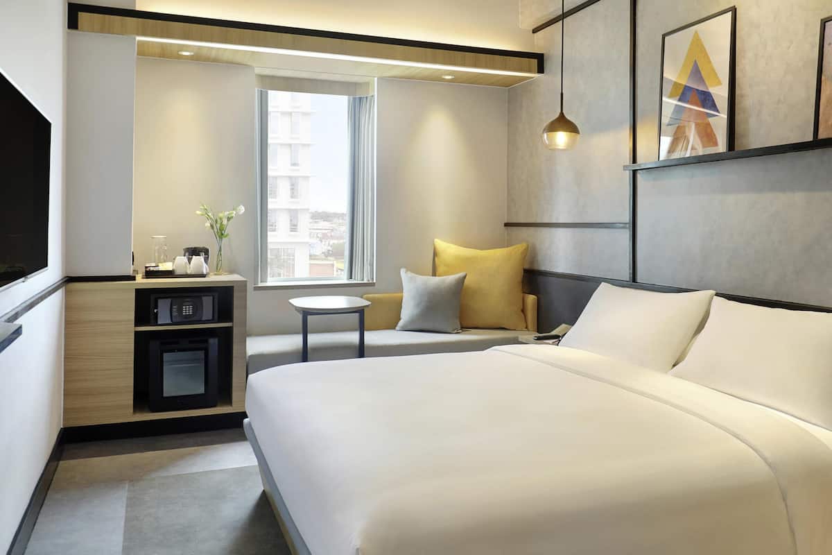 A modern hotel room with a large bed, a small table, a microwave, and a window with a city view.