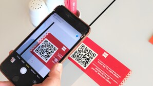 A smartphone displaying a QR code on a red card, with a hand holding the phone. - Ibis Samarinda (Samarinda)