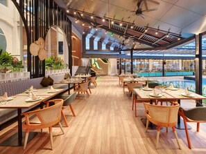 Un restaurante moderno con suelo de madera, techos altos y una piscina visible a través de amplios ventanales.