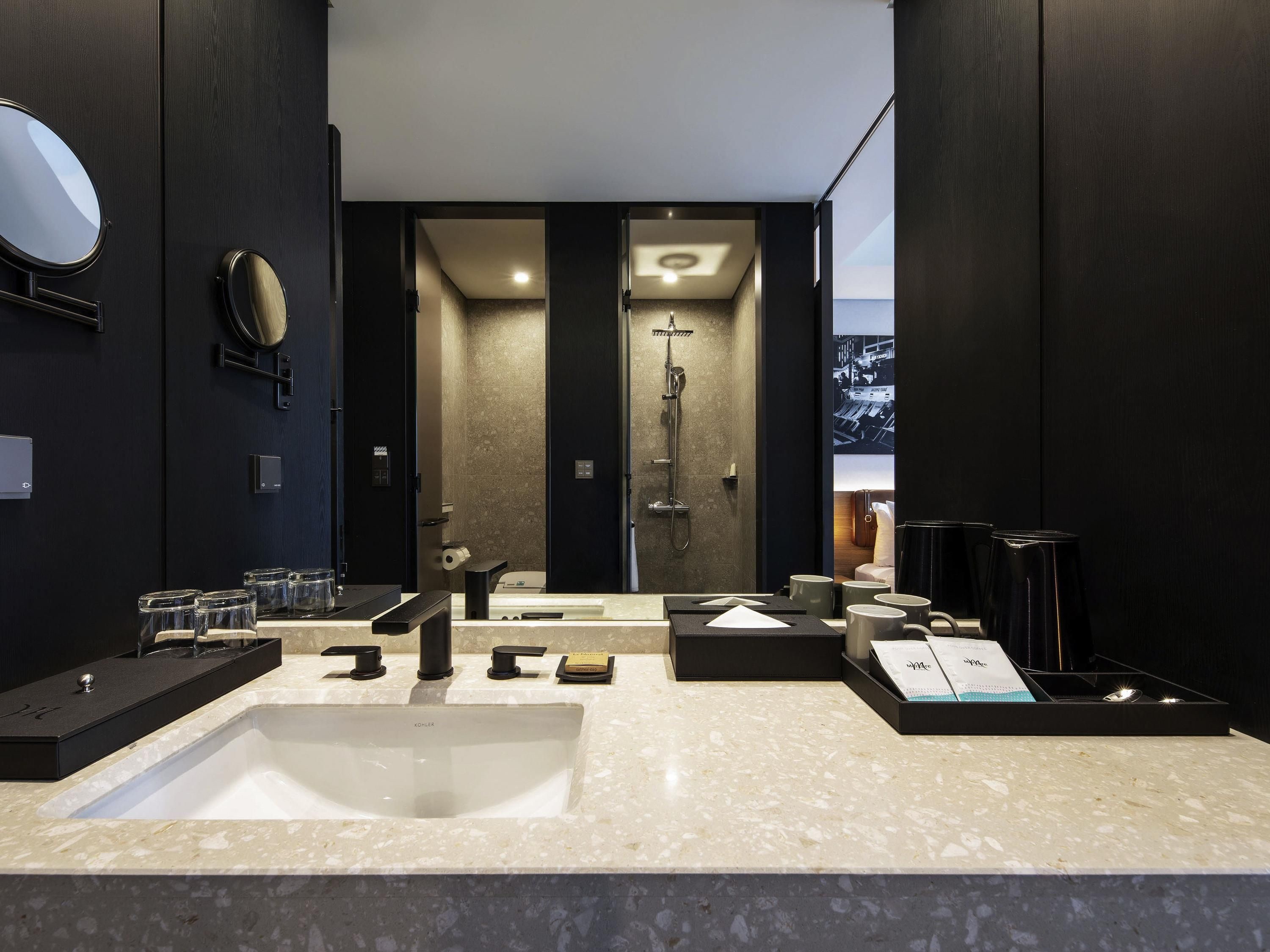 A modern bathroom with a large sink, two mirrors, a shower, and a view of the city through a large window.