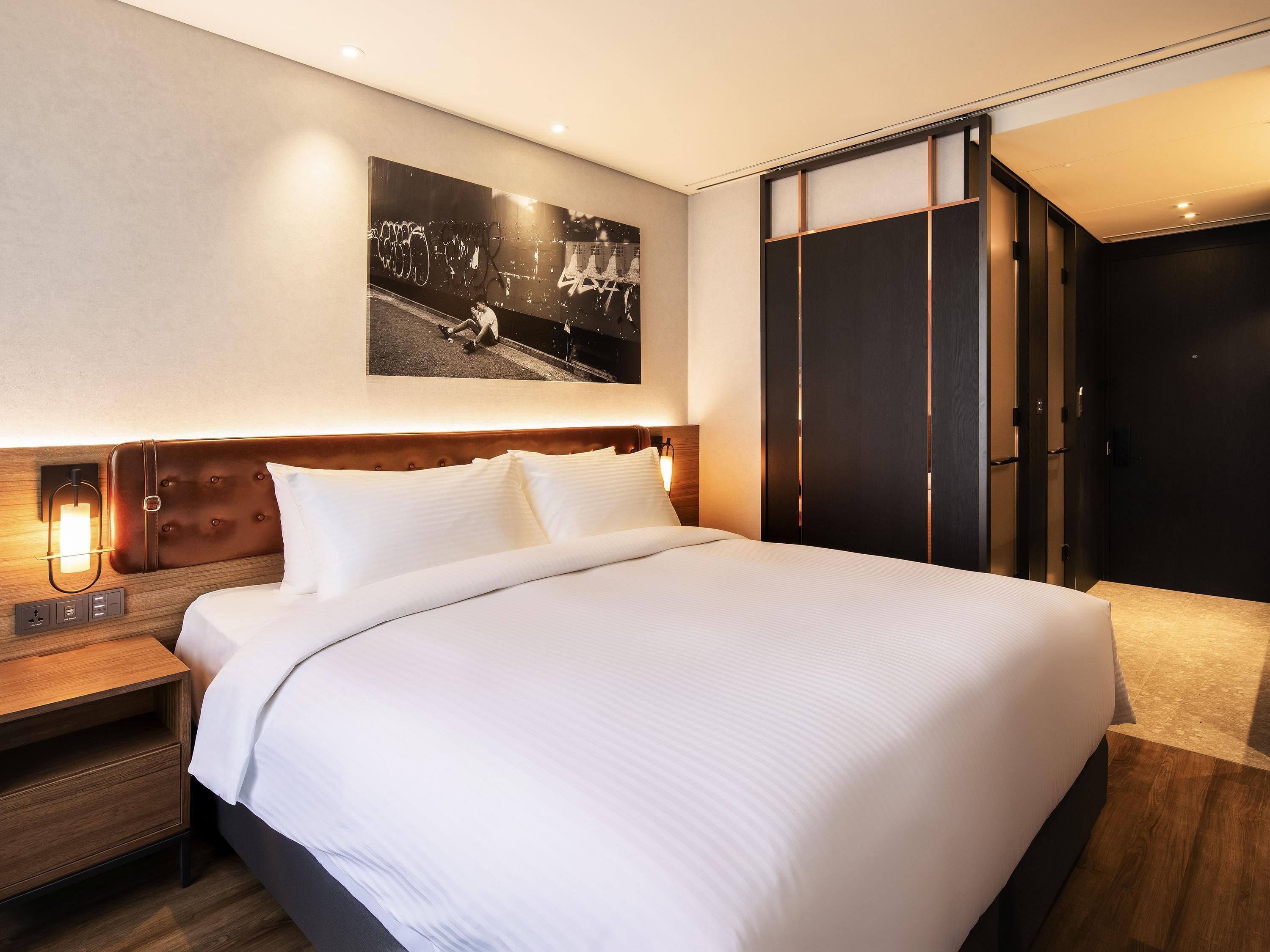 A hotel room with a large bed, a nightstand with a lamp, a wardrobe, and a wall-mounted picture.