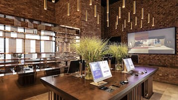 A modern hotel lobby with a brick wall, a reception desk, and a large screen displaying a room.