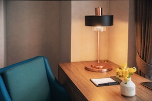 Una mesita de noche de madera con una lámpara moderna, un florero con flores amarillas y un bloc de notas.
