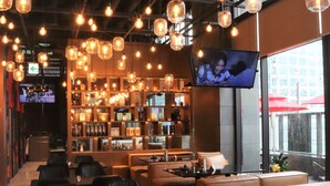 A modern restaurant interior with hanging light fixtures, a bar area, and a television screen. - Mercure Ambassador Seoul Hongdae (Seoul)