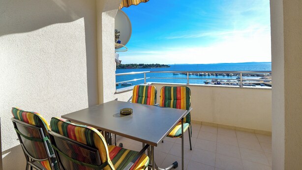 A balcony with a table and chairs, a view of the sea, and a pool area in the background. - Beautiful sea View Apartment (Zadar)