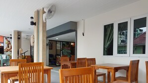 Ein großzügiger Innenbereich mit Holztischen und -stühlen, einem Deckenventilator und Blick ins Freie durch ein Fenster.