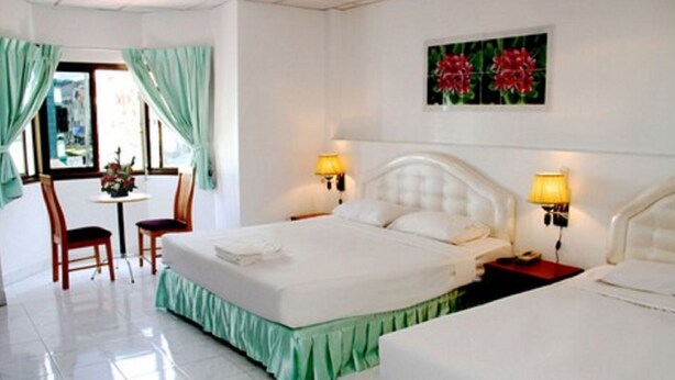 Ein Hotelzimmer mit einem Bett, zwei Nachttischen mit Lampen, einem Sessel, einem kleinen Tisch mit Blumenvase und einem Bild an der Wand.