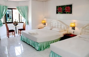 A hotel room with a bed, two bedside tables with lamps, a chair, a small table with a vase of flowers, and a painting on the wall. - Welcome Inn Hotel Karon Beach (Karon)