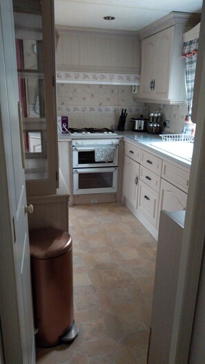 A compact kitchen with a gas stove, oven, and a trash bin.
