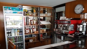 Une cuisine équipée d’un réfrigérateur rempli de boissons, d’étagères où sont rangés les condiments et d’une machine à café.