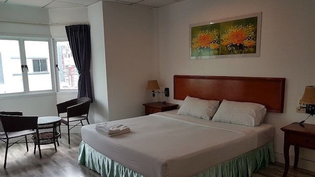 Une chambre d’hôtel avec un grand lit, un bureau, deux chaises, une fenêtre avec des rideaux et un tableau au mur.