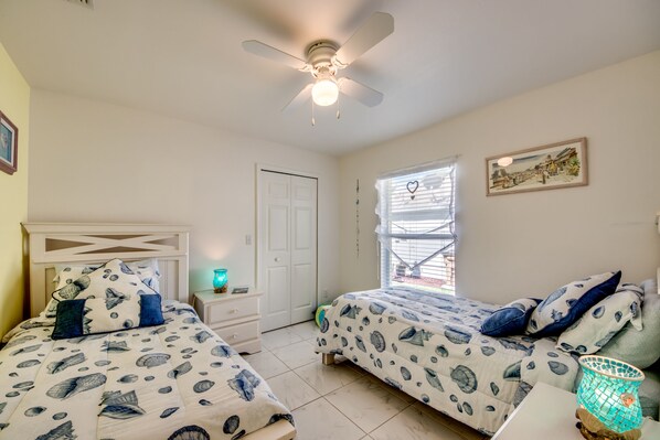 A bedroom with two beds, a ceiling fan, a window with blinds, a door, and a wall-mounted picture.